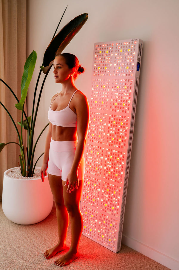 The Radiance960 full body red light panel used by a lady standing in bedroom with the LEDs glowing on the back of her body.