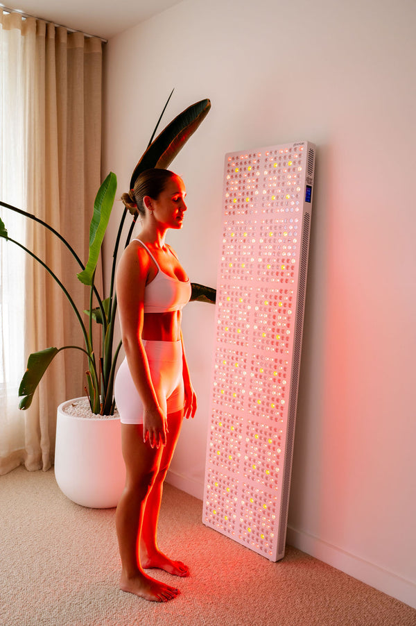 The Radiance960 full body red light panel used by a lady standing in bedroom with the LEDs glowing on the side of her body.