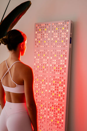 The Radiance960 full body red light panel being used by a lady in bedroom with the LEDs glowing on her body.