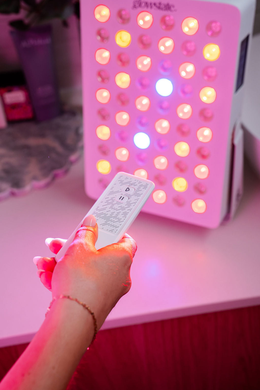 The Radiance60 red light panel placed on a benchtop, glowing LEDs shine as she uses the remote control.