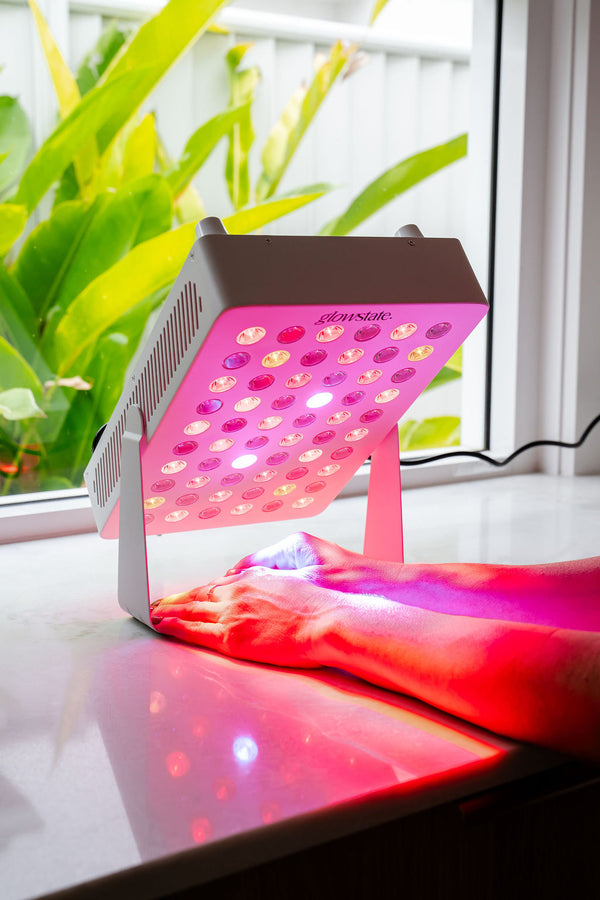The Radiance60 red light panel used by a lady, the panel placed on benchtop, glowing LEDs shine on her wrists.