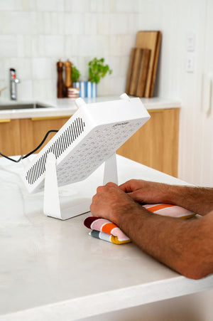 The Radiance60 red light panel about to be used by a man on his wrists, the panel placed on benchtop.
