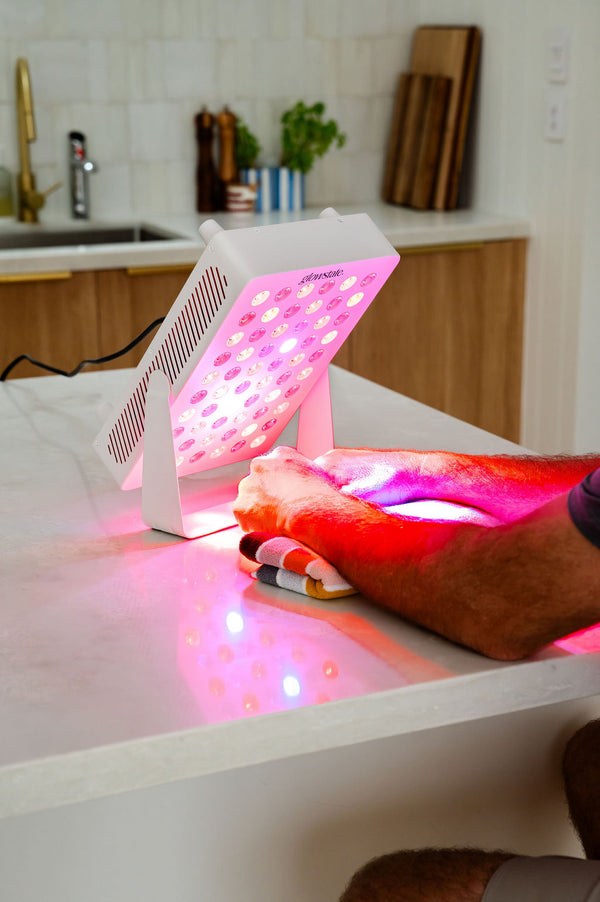 The Radiance60 red light panel used by a man, the panel placed on benchtop, glowing LEDs shine on his wrists.