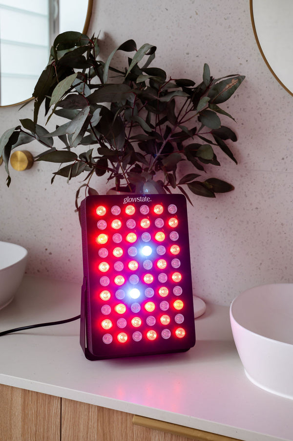 Radiance60 red light panel has a black frame and is sitting on the bathroom benchtop, the LEDs are glowing