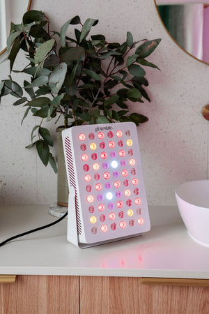 Radiance60 red light panel has a white frame and is sitting on the bathroom benchtop, the LEDs are glowing