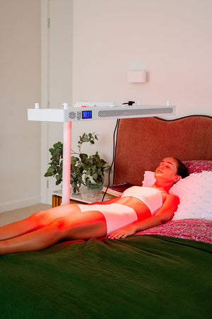 The Radiance300 red light panel is mounted on a stand and positioned over a lady on the bed, LEDs are glowing