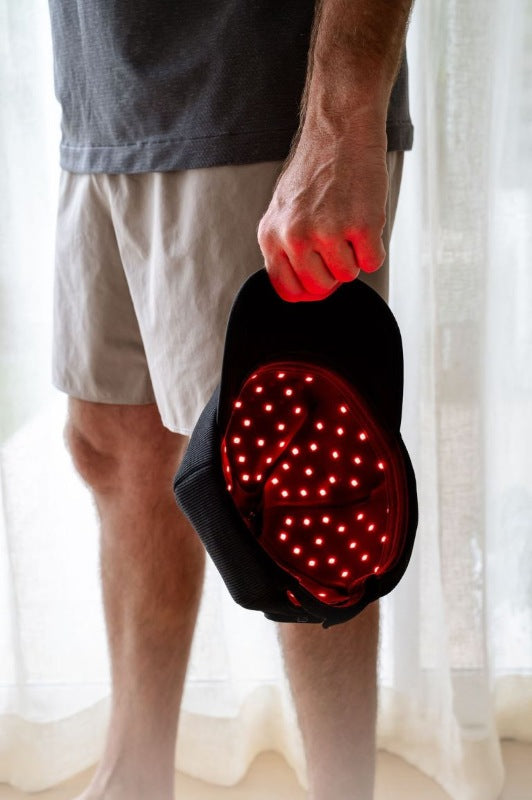 The Halo red light therapy cap held by man's side showing the inside of cap with LEDs glowing, image fades at the bottom.