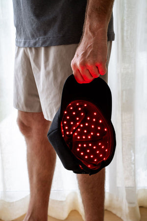 The Halo red light therapy cap being held by man's side showing the inside of cap with LEDs glowing.