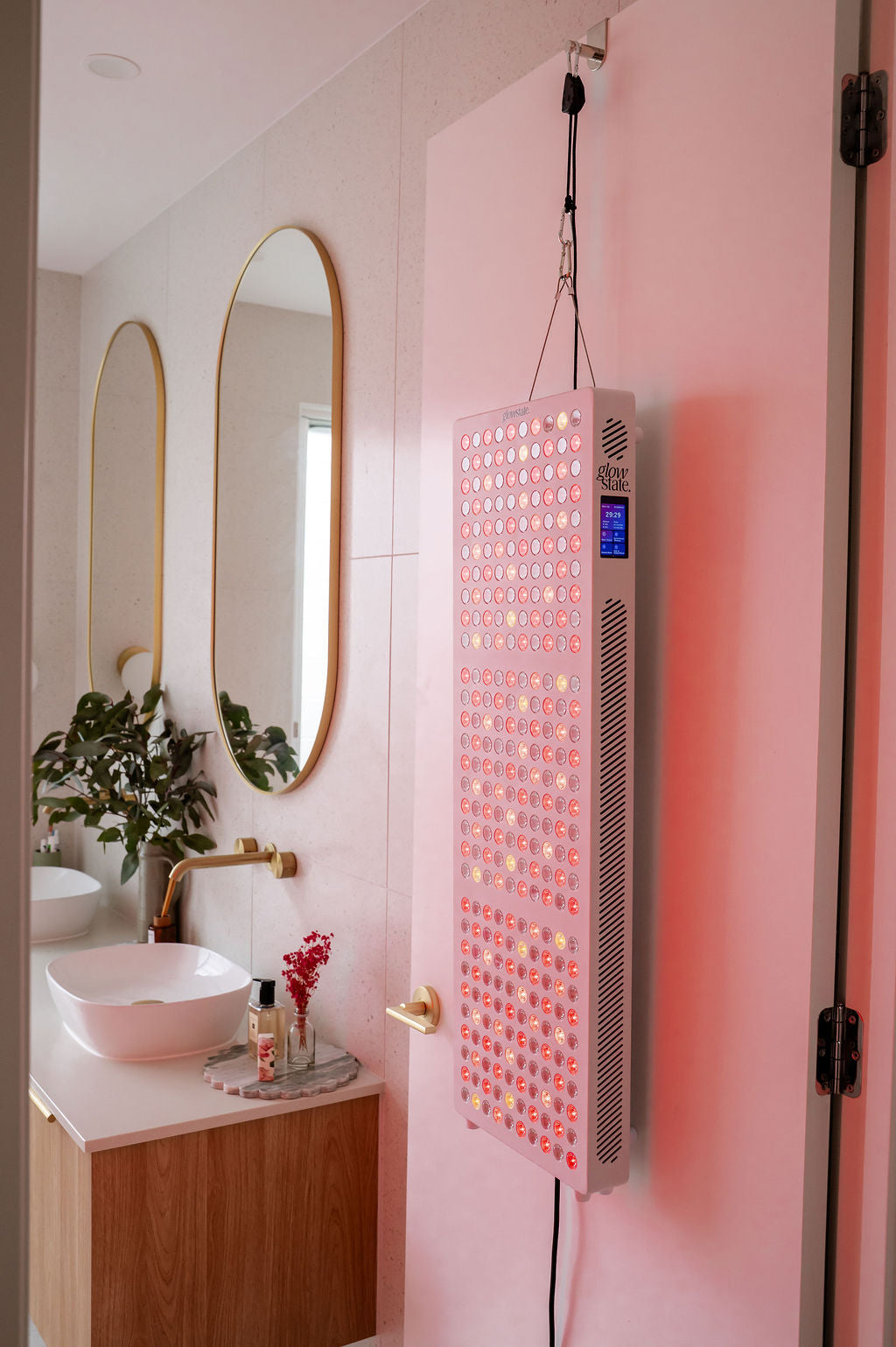 Radiance300 red light panel shown in bathroom with LEDs glowing, the panel is on the height adjustable door hanging kit
